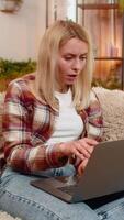 Young adult woman checks email on laptop while sitting on home sofa and sighs in disappointment from bad news. Blonde girl looks discouraged and tense, processing negative online information quietly. video