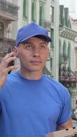 Focused male courier delivering pizza in a vibrant city while calling his client video
