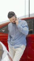 Charming man joyfully talking on his smartphone while selecting a new car at the dealership video