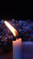 Vertical shot of a burning candle in a dark setting, the glowing flame and colorful bokeh background video