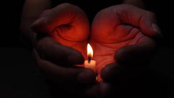 Hands Protecting a Burning Candle from wind in a Dark and Peaceful Setting. The candle flame illuminates the palms, symbolizing the bitterness of loss, death, and grief. video