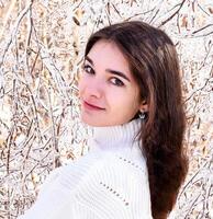 Portrait of a young Russian woman in white sweater looking at camera next to frozen branches of birch trees, covered with ice. Winter forest in Russia photo