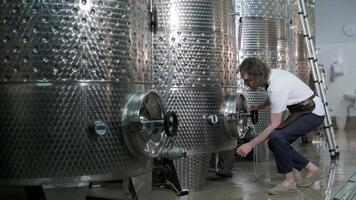 A happy successful farmer or winemaker is walking in the middle of wine tanks and checking a fermentation grade of high quality wine production in a modern winemaking facility or winery. 9 video