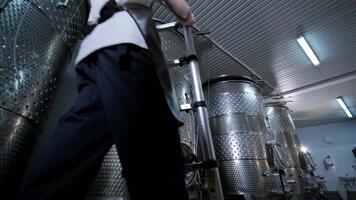 A happy successful farmer or winemaker is walking in the middle of wine tanks and checking a fermentation grade of high quality wine production in a modern winemaking facility or winery. video