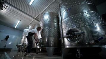 A happy successful farmer or winemaker is walking in the middle of wine tanks and checking a fermentation grade of high quality wine production in a modern winemaking facility or winery. 6 video