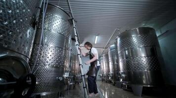A happy successful farmer or winemaker is walking in the middle of wine tanks and checking a fermentation grade of high quality wine production in a modern winemaking facility or winery. 4 video