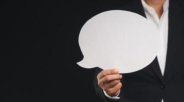 Close-up of a businessman holding a blank white speech bubble while standing on a black background. photo