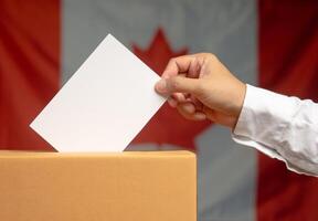 Hand voter holding ballot paper putting into the voting box at place election against the Canada flag background photo