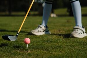 Golf swing practice with a pink ball on a grassy course in bright sunlight featuring a player in comfortable attire and shoes photo