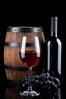 Red Wine Glass with Bottle Grapes and Wooden Barrel on Black Background photo