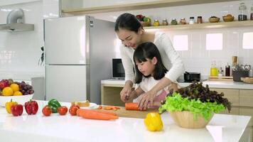Asian mother teaching daughter how to slice carrots in modern kitchen. video