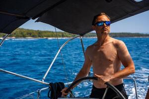 Man with bare torso steering a yacht on the open sea on a sunny day. Concept. summer vacation, yachting, sea travel. High quality photo