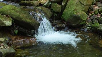 A waterfall cascades down a mountain river, tumbling over rugged stones and creating white foam. Surrounded by rocky terrain and lush greenery, the rushing water adds energ video