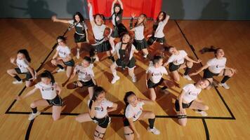 A dynamic dance group performing in a gymnasium, showcasing synchronized movements and energetic poses. The dancers wear matching outfits, creating a vibrant atmosphere. video