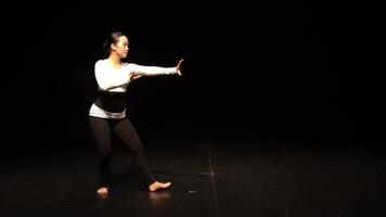 A dancer performing on stage with a spotlight, wearing a black and white outfit. The background is dark, emphasizing the dancer's movements and expressions. video
