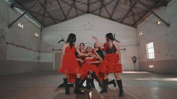 A group of young women in red dresses dancing energetically in an industrial-style hall with high ceilings and large windows. video