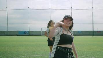 A vibrant dance scene on a sports field featuring three dancers in stylish outfits. The foreground dancer is in motion, creating a dynamic atmosphere video