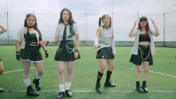 A group of five young women dancing energetically on a sports field, wearing stylish outfits. The scene captures a lively and dynamic atmosphere, with blurred motion indicating movement. video