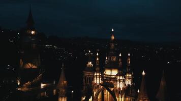 A nighttime view of a beautifully illuminated castle or palace with intricate architecture, surrounded by dark hills and distant lights. The scene evokes a sense of mystery and enchantment. video