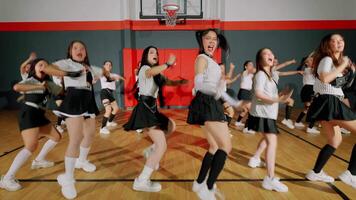 A group of young women performing a synchronized dance routine in a gymnasium. They wear matching outfits with striped tops and skirts, showcasing energetic movements video