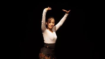 A graceful dancer performing on stage with dramatic lighting. The dancer wears a white long-sleeve top and a black skirt with intricate patterns, showcasing elegance and poise. video