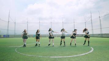 A group of six dancers performing in unison on a soccer field, showcasing energetic choreography. They wear stylish outfits and are positioned in a circular formation video