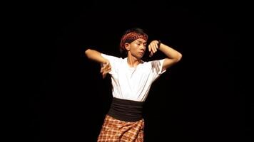 A young male dancer performing on stage with dramatic lighting. He wears a traditional outfit and a headband, showcasing a dynamic pose that conveys energy and expression. video