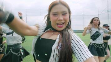 A group of six dancers performing a choreographed routine on a green turf field. They are dressed in stylish outfits, showcasing a mix of skirts and sporty attire video