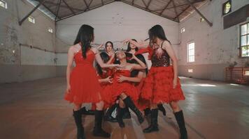 A group of six dancers in red dresses performing a choreographed routine in an industrial space. The dancers exhibit dynamic poses, showcasing energy and synchronization. video