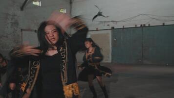 A group of dancers performing a choreographed routine in a spacious indoor setting. They wear stylish outfits with fringes and are captured mid-movement, showcasing energy and synchronization. video