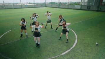 A group of six young women performing a dance routine on a soccer field. They are dressed in matching outfits with skirts and boots, showcasing energetic movements video