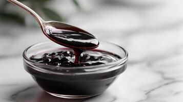 Spoonful of blackberry jam dripping into glass bowl photo