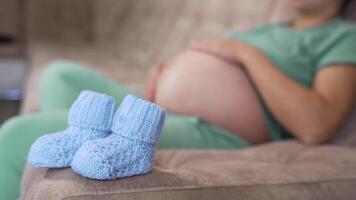 Beautiful knitted socks for future baby. New blue socks on blur background of expectant mother lying on a sofa. Pregnancy time. video