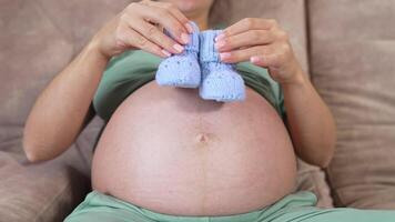 Belly of a pregnant girl. Future mother playing with knitted baby socks on her bare stomach. Concept of health during pregnancy. Close-up. video