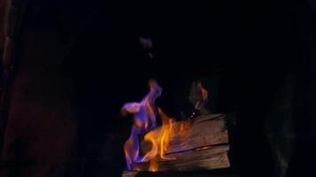 Blue and yellow fire flame burning in a stone fireplace. Wooden logs are burning in darkness. Cozy and warm atmosphere. video