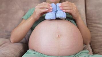 Bare stomach of a future mother. Pregnant woman playing with little knitted socks on her belly lovingly. Close-up. video