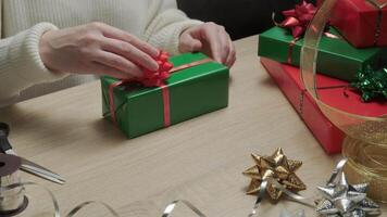 Person Wrapping Festive Christmas Gifts with Red Bows on Wooden Table in Cozy Indoor Setting video