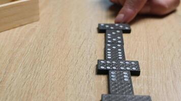 Close-up of a person placing black domino tiles on a wooden table in casual indoor setting video
