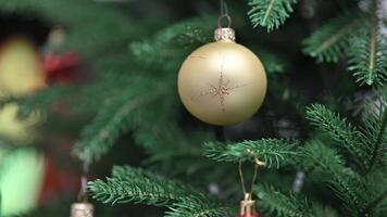 Close-up of Elegant Golden Christmas Ornament Hanging on a Festively Decorated Green Pine Tree with Colorful Lights video