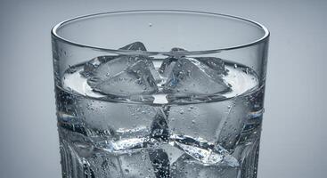 Close-up glass with chilled water, cracked ice, grey background, realistic. photo