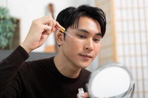 Skincare Routine. Young man applying serum for glowing skin. photo