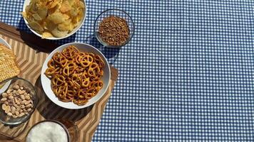 A variety of snacks like pretzels, chips, and nuts on a checkered tablecloth evoke casual gatherings and picnics, ideal for summer outings video