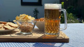 A refreshing glass of beer with snacks, perfect for a summer picnic, featuring crisps and nuts on a sunny day video
