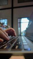 Time lapse of side view close-up man's hands typing on keyboard on laptop at table in cafe on holiday. Concept of working outdoors, comfortable workspace or freelance career, footage vertical video