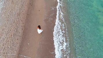 Aerial view of woman in white dress walking barefoot along beach near rope line video