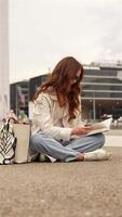 Woman reading book sitting on ground in business district video