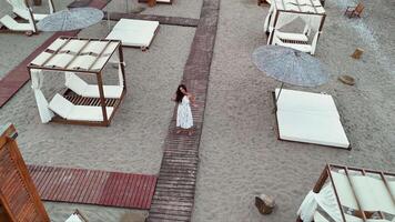 Woman walking on boardwalk between cabanas on sandy beach video