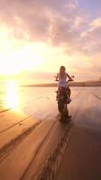 FPV drone shot of woman riding motorcycle along tropical beach during golden sunset, creating cinematic, free-spirited atmosphere. Concepts of freedom, adventure, and slow travel lifestyle. video