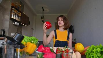Beautiful young caucasian housewife woman throwing sweet red pepper up. Female nutritionist with healthy vegetables in kitchen. camera movement around. Looking at camera and smiling video