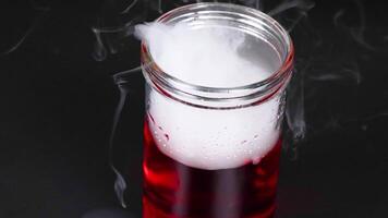 A sequence showing dry ice reacting in a red liquid, creating fog and bubbles in a glass beaker video